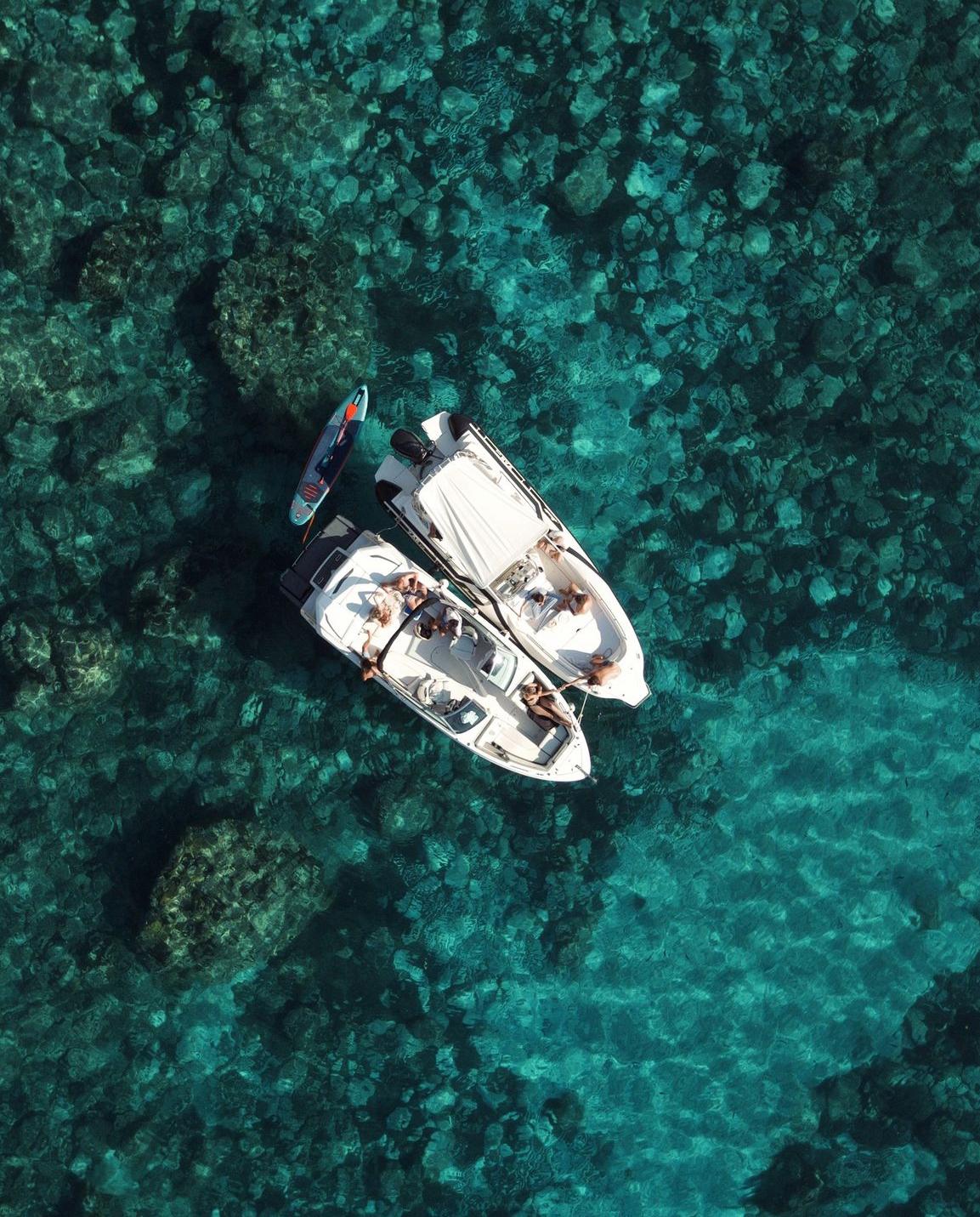 Dos barcos juntos en una cala turquesa con tabla de paddle surf