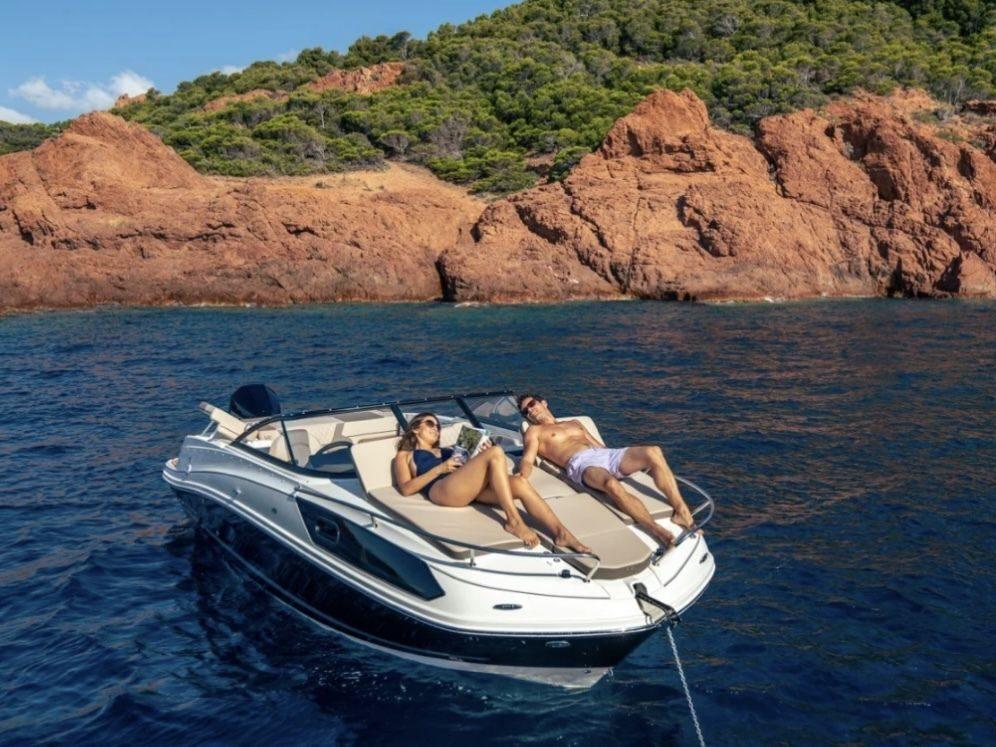 Pareja tomando el sol en el solárium del Bayliner VR6 fondeado frente a la costa rocosa