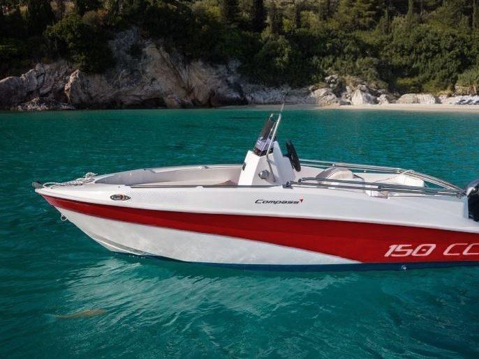 Lancha Compass 150 CC roja y blanca fondeada frente a una cala con playa